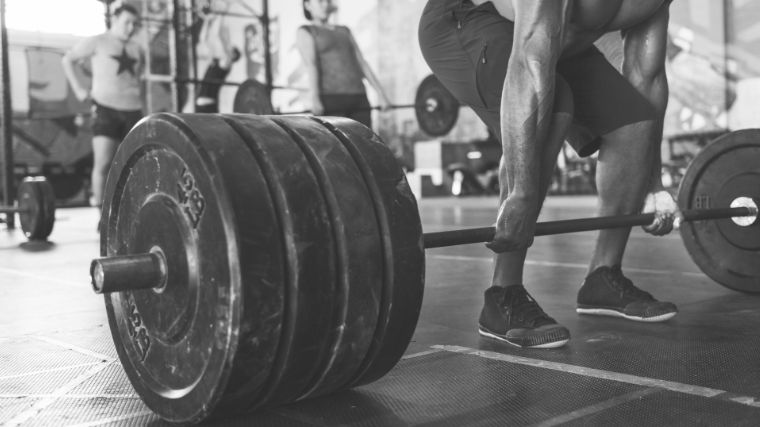 Man in black shorts gripping a loaded barbell resting on the floor with both hands