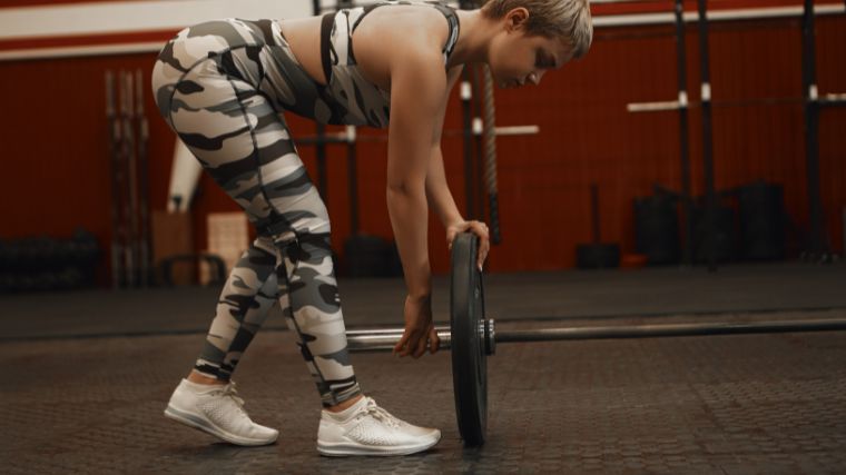 Person wearing white and black camouflage leggings and sports bra adding a weight plate onto a barbell 