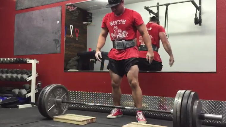A person wearing a red Westside Barbell shirt and lifting belt stares down at a deficit deadlift setup.
