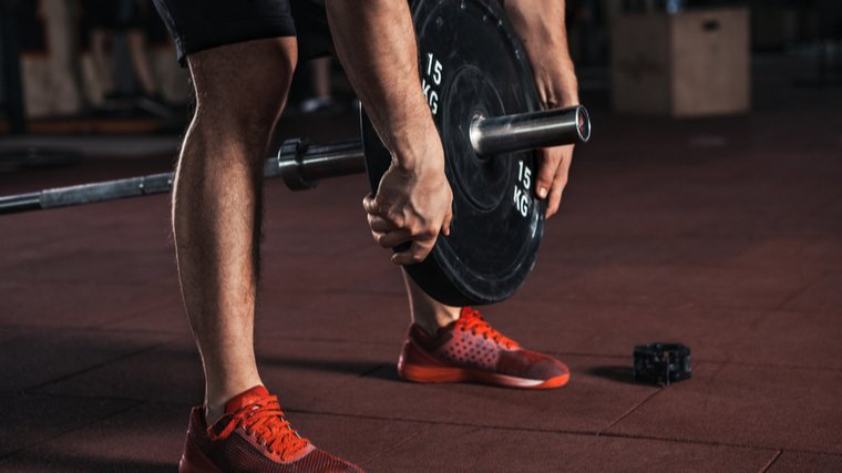 A person wearing red shoes unloads a weight plate from a barbell.