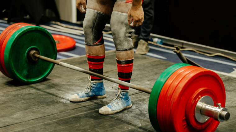 A person wears knee sleeves and deadlifting socks prepares to lift a barbell.