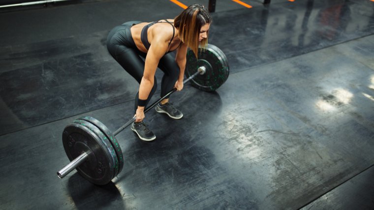 A person wears a sports bra and training pants as they set up to lift a loaded barbell from the floor.