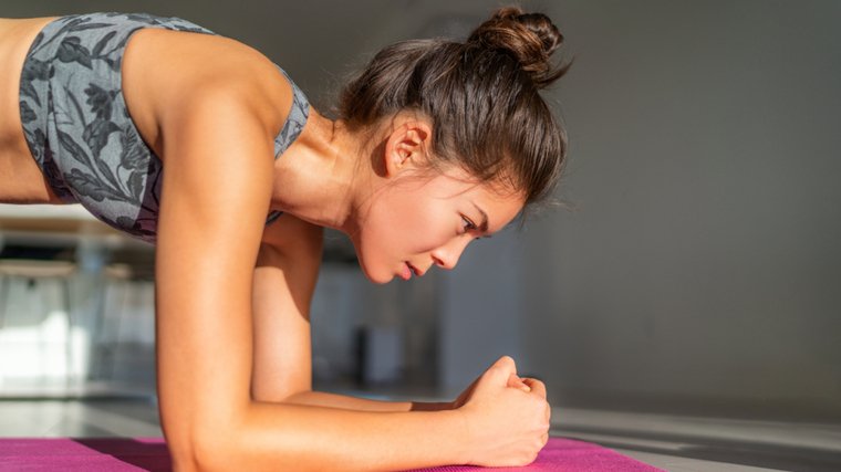 A close-up image shows a person with their hair in a bun performing a forearm plank.