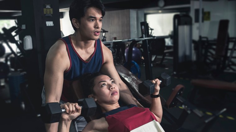 One person spots another while they perform an incline dumbbell bench press.